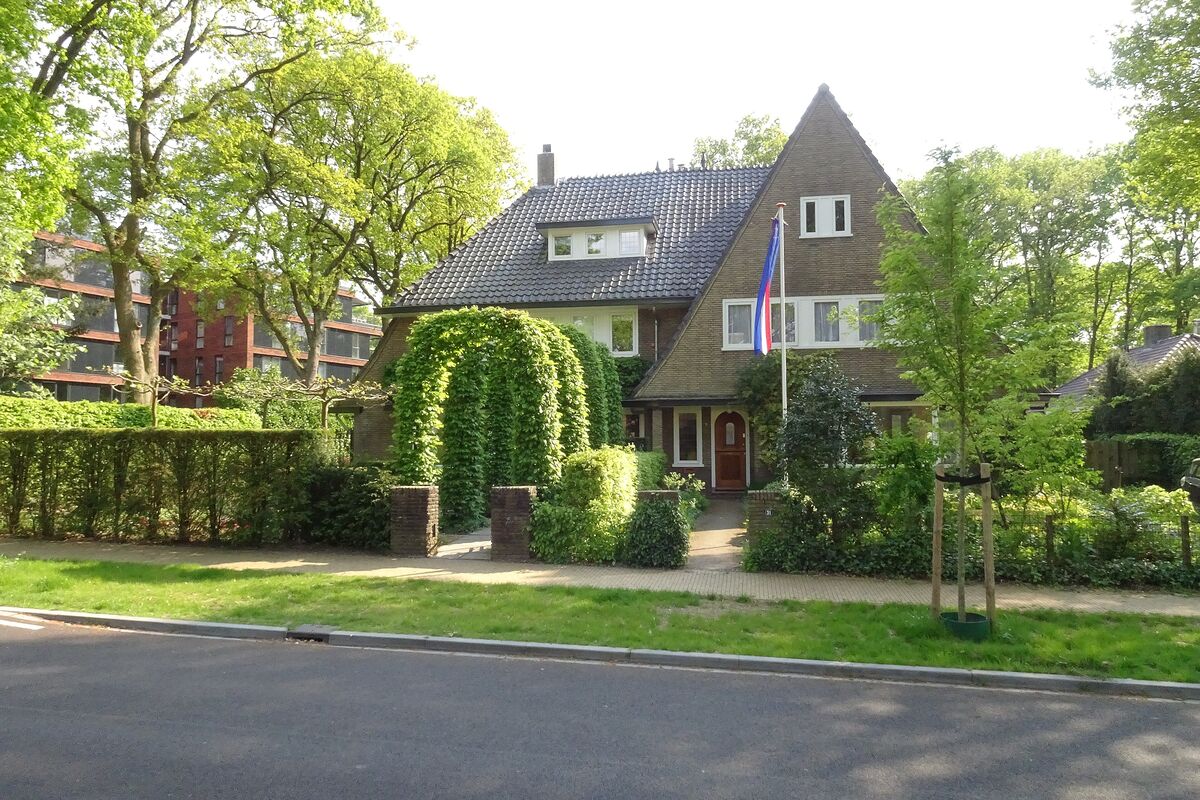 Een voortuin met geschoren hagen, een haagboog en een gazon voor een woning