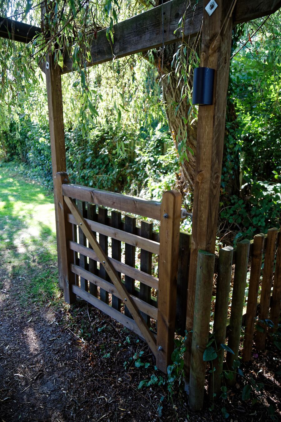 Een houten tuinpoort onder een pergola met een pad erachter